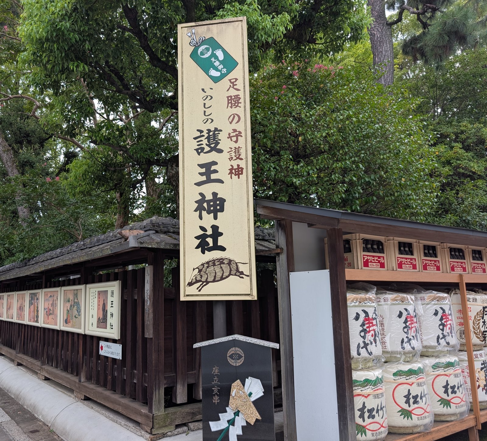 社頭の看板「足腰の守護神 いのししの護王神社」と、脇に並ぶ酒樽(2026-08-22 撮影)